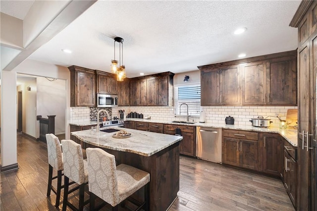 kitchen featuring sink, hanging light fixtures, appliances with stainless steel finishes, an island with sink, and decorative backsplash