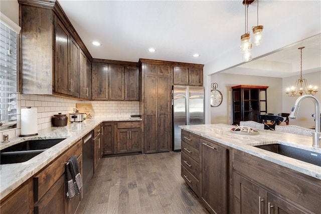 kitchen with dark hardwood / wood-style floors, pendant lighting, sink, stainless steel appliances, and light stone countertops