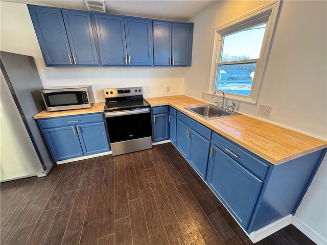 kitchen with dark wood-type flooring, sink, appliances with stainless steel finishes, and blue cabinetry