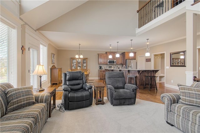 living room featuring an inviting chandelier, crown molding, light hardwood / wood-style flooring, and a high ceiling