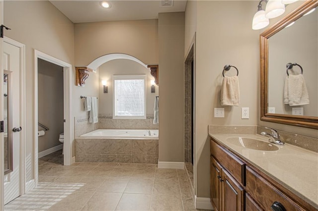 bathroom featuring vanity, a relaxing tiled tub, tile patterned floors, and toilet