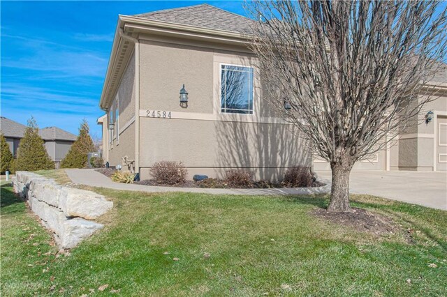 view of side of home featuring a lawn, a garage, driveway, and stucco siding