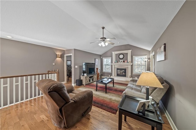 living room featuring a tiled fireplace, vaulted ceiling, ceiling fan, and light hardwood / wood-style flooring