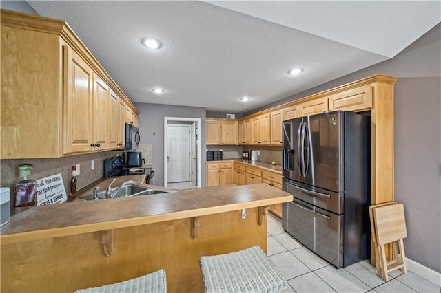 kitchen with light tile patterned flooring, light brown cabinetry, a breakfast bar area, kitchen peninsula, and black appliances