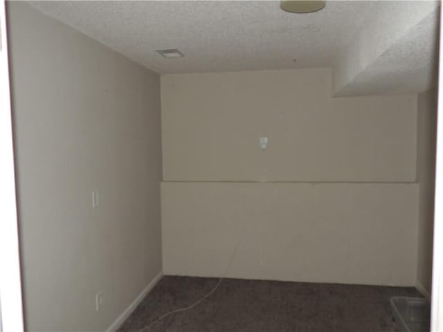 empty room with a textured ceiling and dark carpet