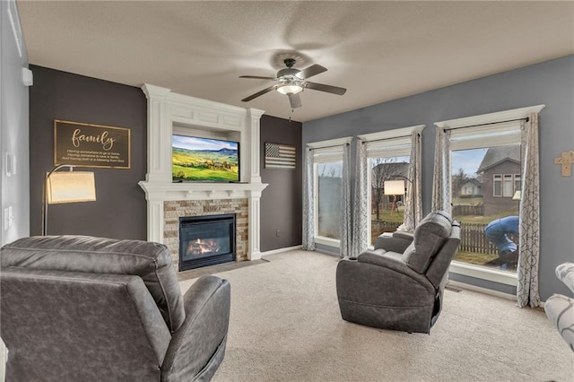 living area featuring a textured ceiling, carpet floors, a fireplace, a ceiling fan, and baseboards