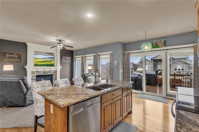 kitchen with a sink, a stone fireplace, stainless steel dishwasher, and light wood finished floors