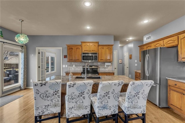 kitchen with tasteful backsplash, visible vents, light wood-style flooring, appliances with stainless steel finishes, and a kitchen island with sink