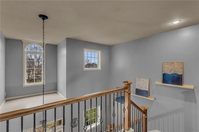 hallway featuring a textured ceiling, plenty of natural light, an upstairs landing, and baseboards