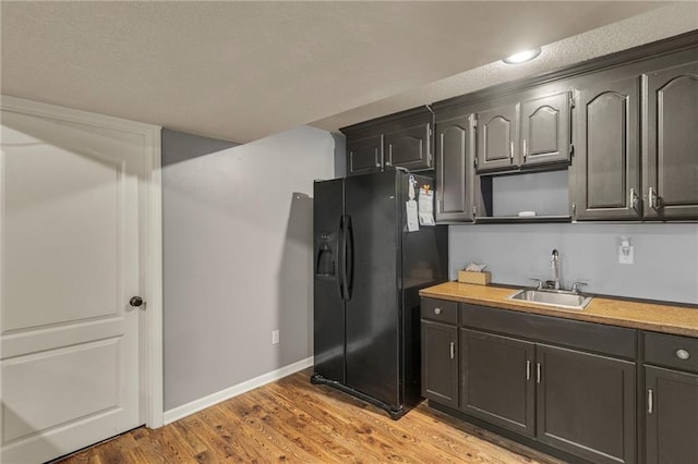 kitchen featuring a sink, black fridge with ice dispenser, baseboards, light countertops, and light wood finished floors