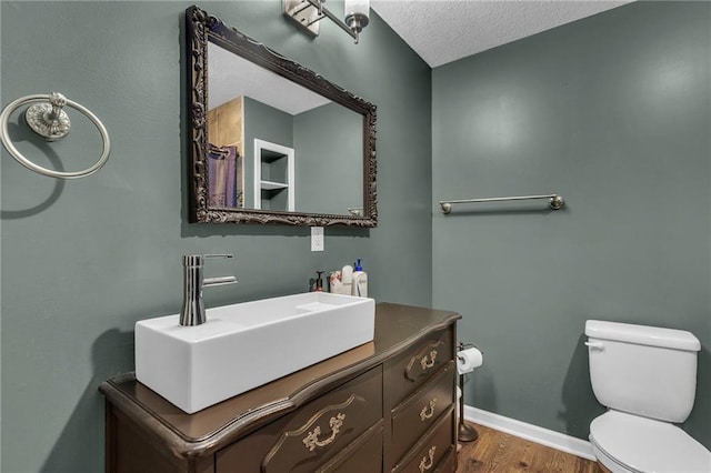 bathroom with a textured ceiling, toilet, wood finished floors, vanity, and baseboards