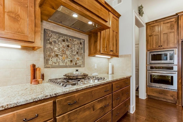 kitchen with wall chimney range hood, appliances with stainless steel finishes, dark hardwood / wood-style floors, light stone countertops, and decorative backsplash