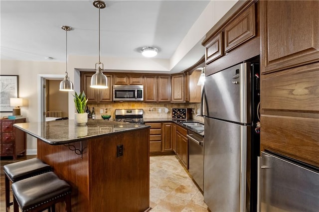 kitchen featuring brown cabinets, appliances with stainless steel finishes, a breakfast bar, and decorative light fixtures