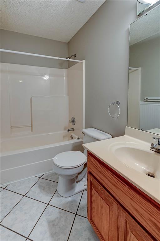 828 SW Harvest Dr, Grain Valley, MO 64029 - full bathroom with a textured ceiling, bathing tub / shower combination, vanity, tile patterned floors, and toilet