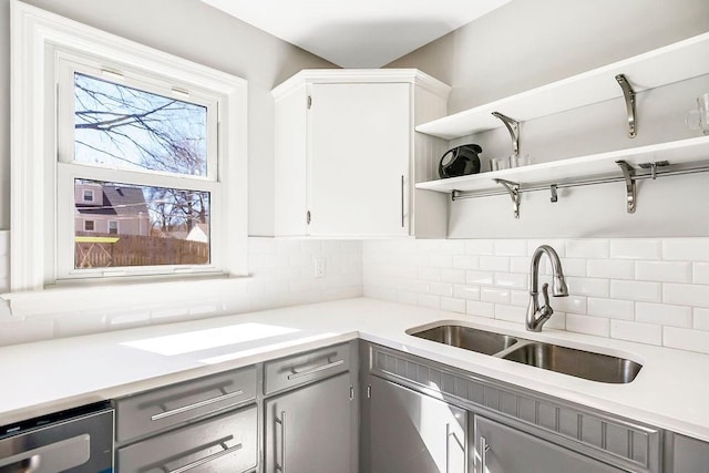 kitchen featuring light countertops, gray cabinets, backsplash, and a sink