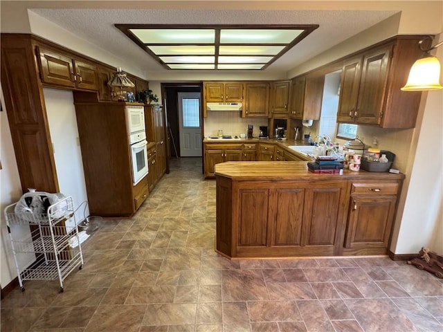 kitchen with sink, white appliances, kitchen peninsula, and a textured ceiling