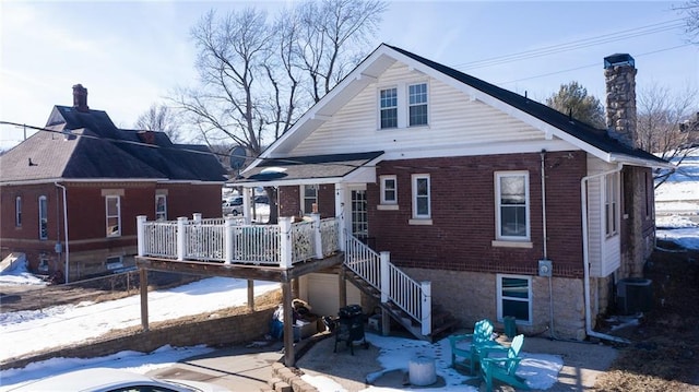 snow covered back of property featuring central AC and a deck