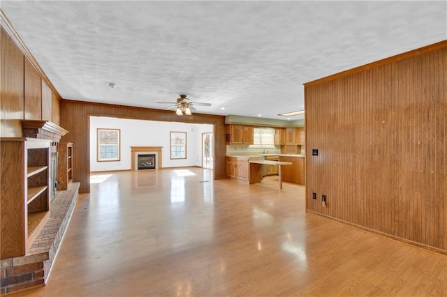 unfurnished living room featuring ceiling fan, wooden walls, light hardwood / wood-style floors, and a textured ceiling