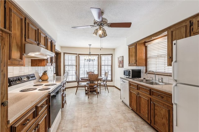 kitchen with sink, pendant lighting, white appliances, ceiling fan with notable chandelier, and backsplash