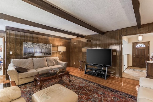 living room featuring hardwood / wood-style flooring, wooden walls, a textured ceiling, and beamed ceiling