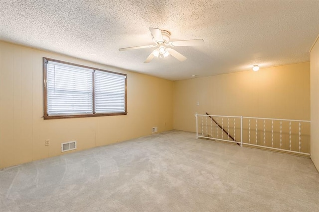 spare room featuring ceiling fan, light carpet, and a textured ceiling