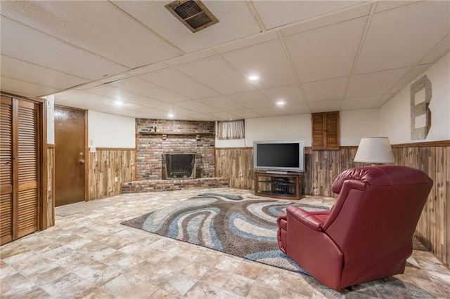 living room featuring a fireplace, a paneled ceiling, and wood walls