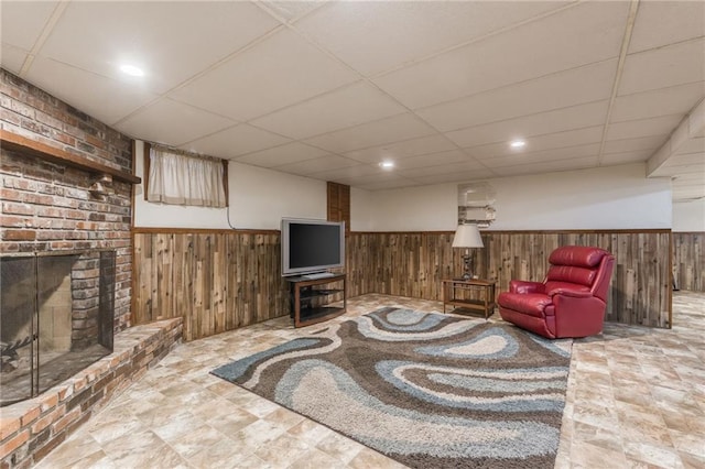 living room with a paneled ceiling, wooden walls, and a fireplace