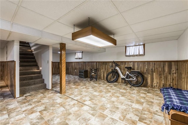 basement featuring wooden walls and a paneled ceiling