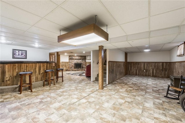 basement featuring a large fireplace, a drop ceiling, and wood walls