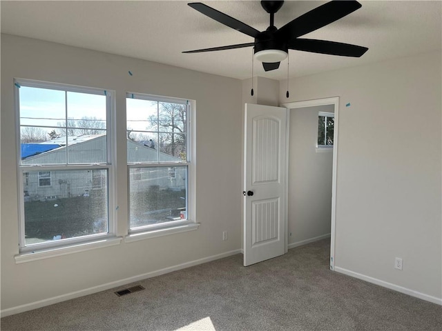 empty room featuring baseboards, a ceiling fan, visible vents, and light colored carpet