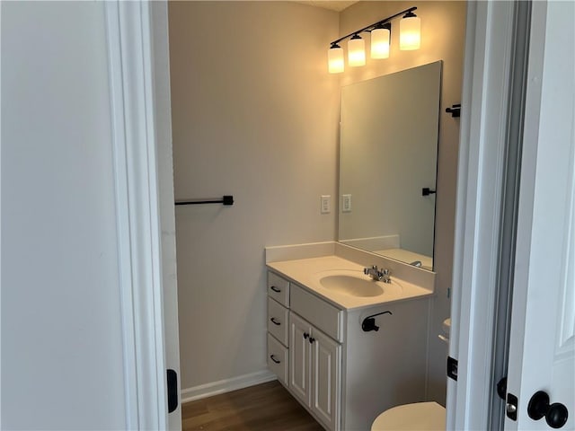 half bath with vanity, baseboards, and wood finished floors