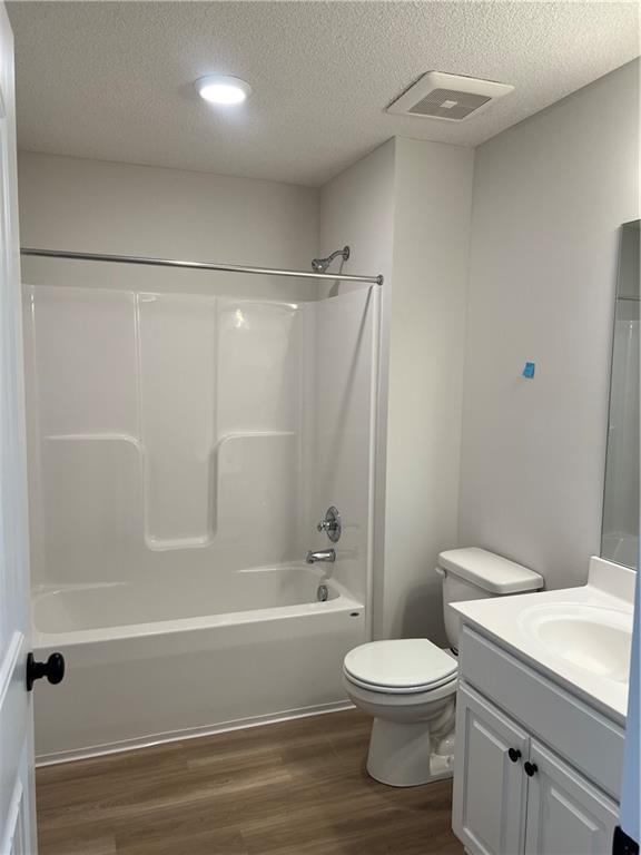 bathroom featuring toilet, wood finished floors, vanity, visible vents, and shower / washtub combination