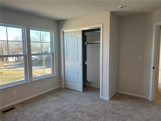 unfurnished bedroom featuring a textured ceiling, a closet, visible vents, and light colored carpet