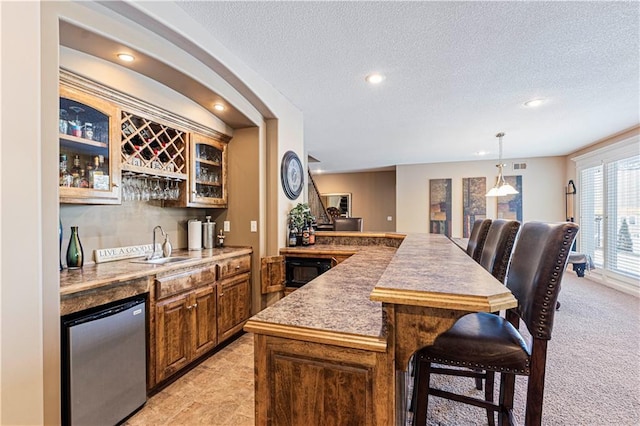 bar featuring sink, stainless steel refrigerator, a textured ceiling, light carpet, and decorative light fixtures