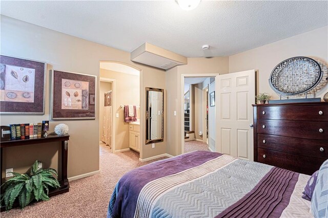 bedroom with light colored carpet, a textured ceiling, and ensuite bath