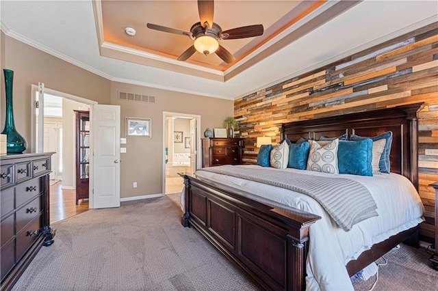 bedroom featuring connected bathroom, wood walls, a raised ceiling, crown molding, and light carpet