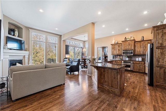 kitchen featuring dark wood-type flooring, a breakfast bar, appliances with stainless steel finishes, decorative backsplash, and dark stone counters