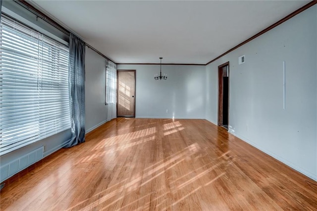 unfurnished room featuring crown molding, light wood-type flooring, and an inviting chandelier