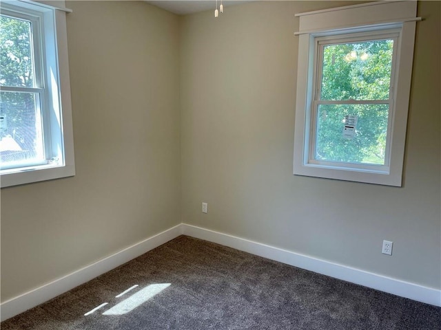 unfurnished room featuring a healthy amount of sunlight, baseboards, and dark carpet