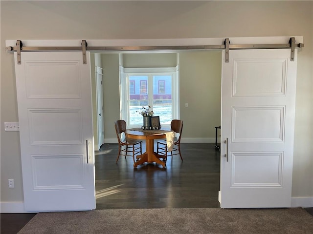 dining area with dark wood-style flooring, baseboards, a barn door, and dark colored carpet