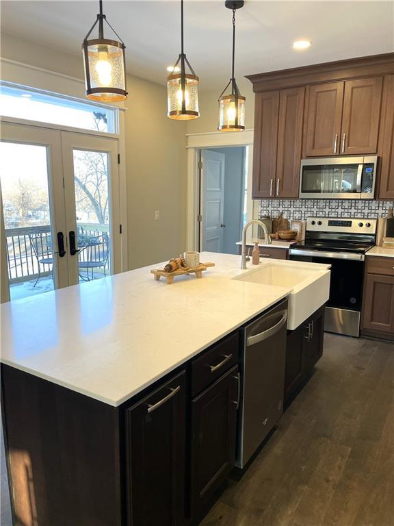 kitchen featuring a center island with sink, light countertops, tasteful backsplash, a sink, and appliances with stainless steel finishes