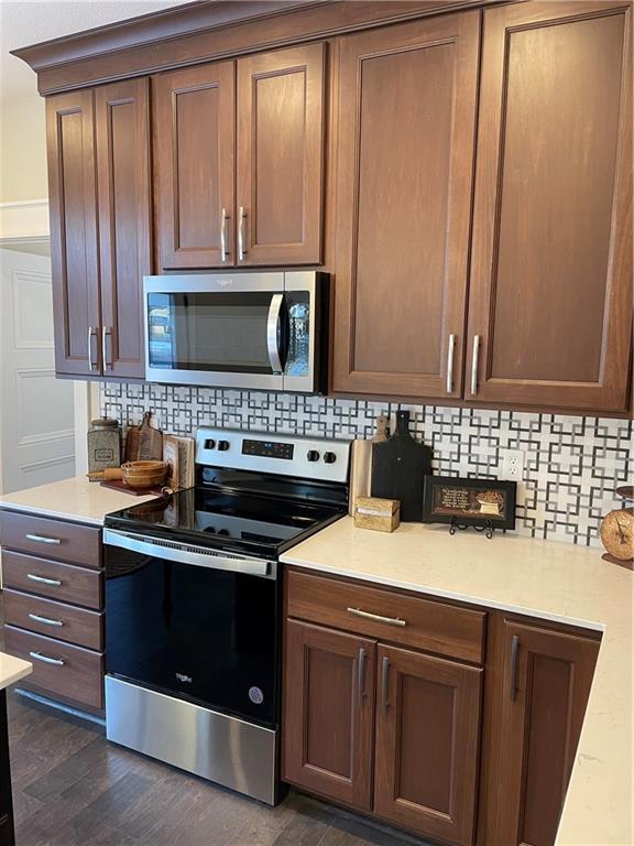 kitchen featuring light countertops, backsplash, appliances with stainless steel finishes, and dark wood-style flooring