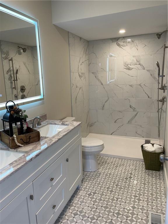 full bath with toilet, visible vents, a marble finish shower, and vanity