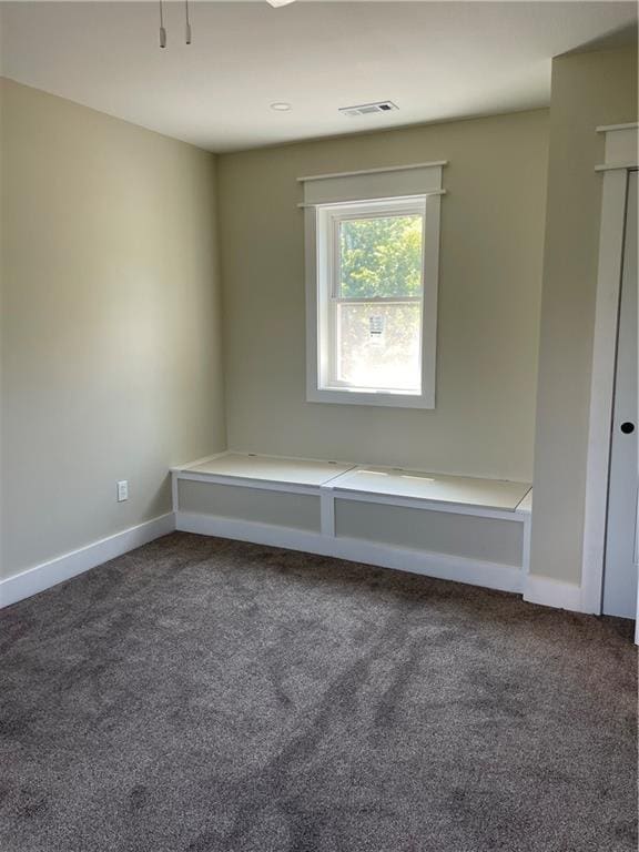 spare room featuring dark colored carpet, baseboards, and visible vents
