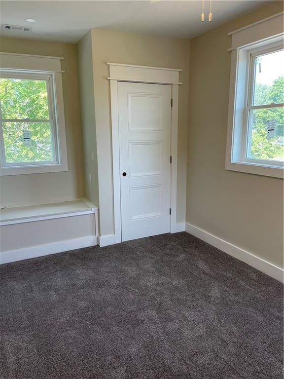 unfurnished bedroom featuring baseboards, multiple windows, dark colored carpet, and visible vents