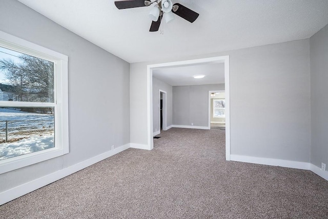 carpeted empty room with ceiling fan and a wealth of natural light