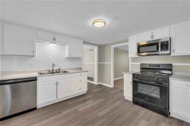 kitchen featuring sink, light wood-type flooring, white cabinets, stainless steel appliances, and backsplash