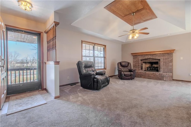 sitting room with ceiling fan, light colored carpet, a raised ceiling, and a brick fireplace