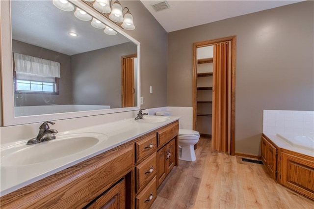 bathroom with tile walls, hardwood / wood-style flooring, vanity, toilet, and a bath