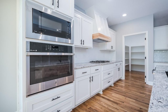 kitchen featuring white cabinets, light stone countertops, custom exhaust hood, and stainless steel appliances